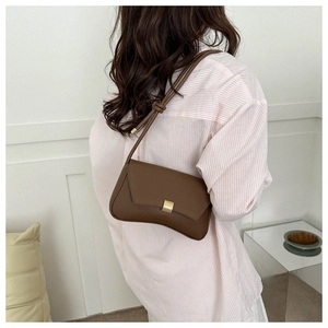 Detail of a dark brown baguette bag with golden buckle on a striped shirt model