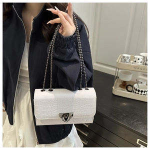 Detail of white crocodile pattern shoulder bag with metal chain on model
