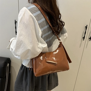 Brown patent leather shoulder bag with glossy finish shown on model in a side view