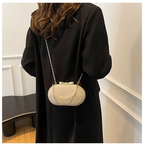 Detail of champagne gold glitter evening clutch bag with bow clasp worn over a black blazer