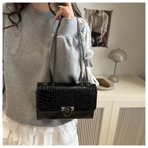 Close-up of black crocodile pattern flap bag with silver chain and metallic buckle detail
