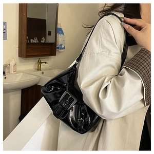 Detail of black patent leather shoulder bag with metallic buckle pockets and Y2K aesthetic
