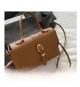 Detail of brown litchi grain leather bag featuring a gold buckle and shoulder strap