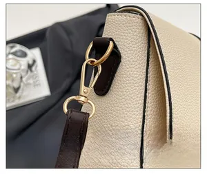 Detailed macro view of polished gold metal hook on off-white lychee grain leather bag
