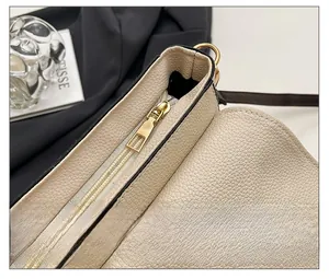 Detail of smooth gold zipper and pebble leather texture on beige crossbody bag