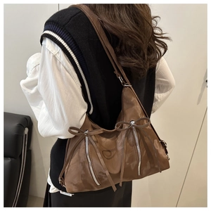 Detail of a brown glossy leather tote bag featuring stylish long ribbon bow accents