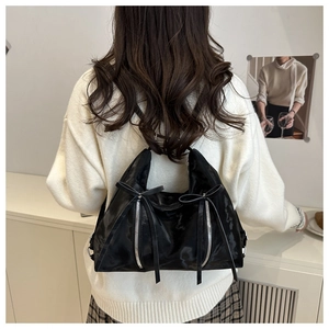 Detail of black glossy tote bag featuring metal zippers and decorative bow ribbons