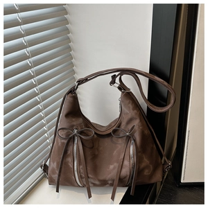 Detail of a brown crescent shoulder bag with glossy nylon finish and decorative bows