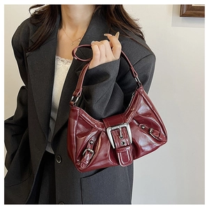 Close-up of glossy wine red leather Y2K shoulder bag with silver buckle and pleated detail