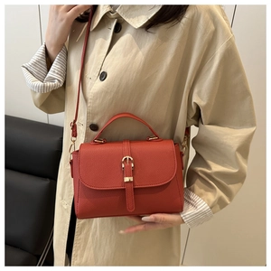Detail of brick red lychee texture leather handbag with gold buckle on a beige trench coat
