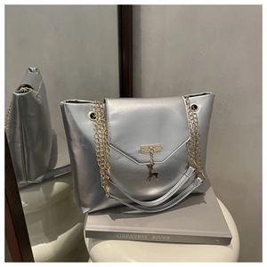 Detail of silver metallic tote bag featuring gold chain straps and a deer pendant charm