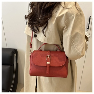 Detail view of red lychee grain leather handbag with gold buckle on a light trench coat