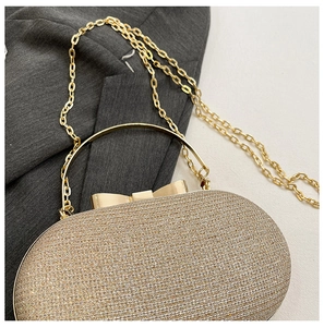 Close-up of champagne gold sequined evening bag with metal handle and bow clasp detail