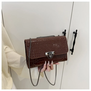 Detail of brown crocodile pattern shoulder bag with silver clasp and metal chain
