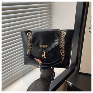 Detail of glossy black tote bag featuring gold chain straps and a deer charm pendant
