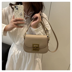 Detail of vintage bronze square lock on a beige saddle bag worn with white dress