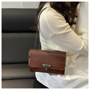 Detail of dark brown faux crocodile leather bag with a metallic chain strap and buckle
