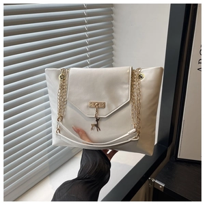 Close-up of white leather tote bag featuring gold deer charm and elegant chain strap