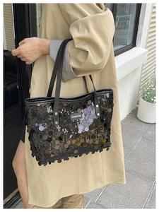 Close-up of black sequined tote bag with Creative Cat label on a beige trench coat