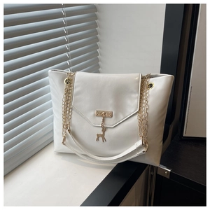 Detail of off-white tote bag featuring a golden chain strap and a deer-shaped metal pendant