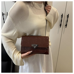 Detail of dark brown crocodile pattern texture and dark grey metal lock on a handbag