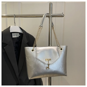 Detail of silver metallic tote bag featuring a golden deer charm and twist-lock closure