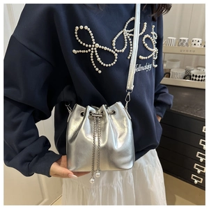 Detailed view of silver metallic bucket bag featuring pearl drawstring and chain strap