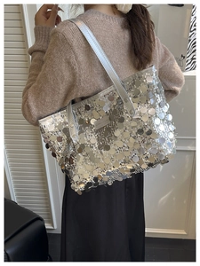 Close-up of a silver sequin tote bag with a Creative Cat label worn on a woman's shoulder