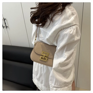 Detail view of a beige crossbody bag with a gold clasp worn over a white lace blouse