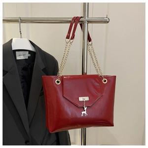 Detail of burgundy glossy tote with gold magnetic clasp and silver deer charm pendant