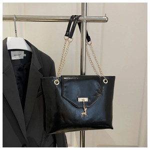 Detail of black patent leather bag with gold chain strap and deer pendant on a hanger