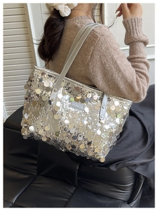 Detail of silver sequin tote bag with chain strap worn by model against neutral background