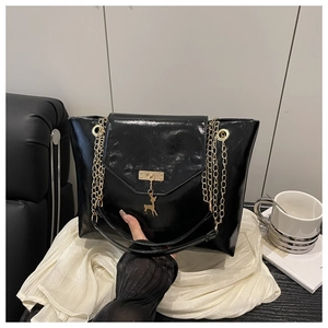 Detail of glossy black tote bag featuring golden deer charm and multi-strand chain strap