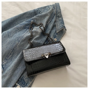 Detail of black crocodile pattern flap bag with metal chain on denim background