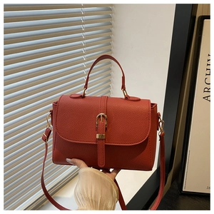 Detailed texture of brick red lychee grain leather handbag with gold buckle and strap