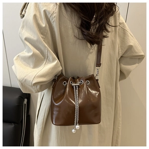 Close-up of brown bucket bag with silver chain drawstring and white pearl charm detail