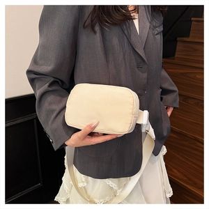 Detail of adjustable strap and plastic buckle on cream nylon crossbody chest bag