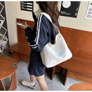 Detail showing wide shoulder strap and blue letter print on beige canvas tote bag