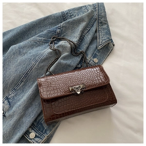 Detailed close-up of dark brown crocodile pattern leather bag with metal chain on denim