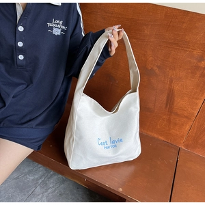 Sac fourre-tout en toile blanche avec texte bleu tenu par un mannequin sur un banc