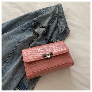 Detail showing pink crocodile embossed texture and dark grey metal chain strap on bag