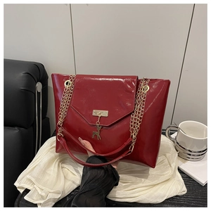 Detail of dark red glossy leather tote with golden chain and deer charm on white fabric