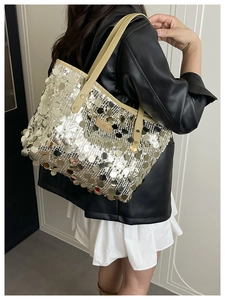 Detail of silver sequin tote bag with beige leather strap on model in black leather jacket