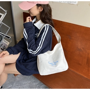 Detail of white canvas tote bag with blue C'est lavie embroidery on the shoulder