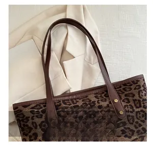Detail of leopard print tote bag with brown leather handles and golden metal rivets