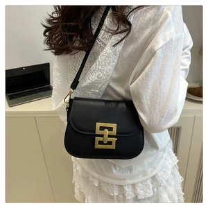 Detail of black leather crossbody bag featuring a golden geometric clasp and matte finish