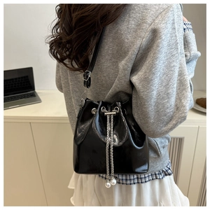 Detail of glossy black drawstring bucket bag featuring silver chain and pearl charms