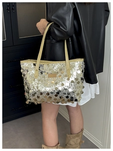 Detail of shimmering gold sequin tote bag with leather handles and metallic texture