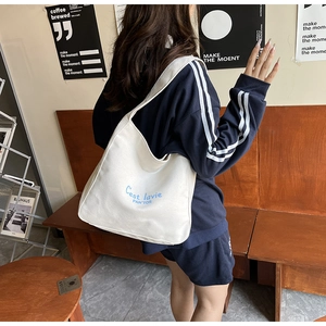 Gros plan d'un cabas en toile crème avec broderie bleue porté par un mannequin femme