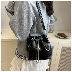Detail of black glossy bucket bag with silver chain drawstring and pearl accents